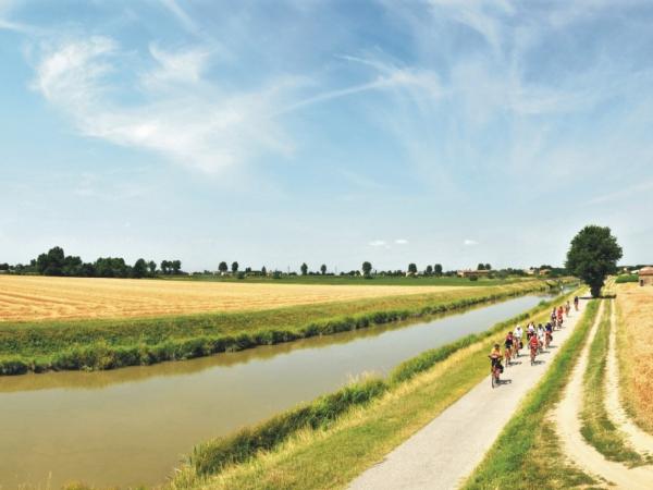 Radfarergruppe unterwegs am von Weizenfeldern gesumten Kanal in der Po-Ebene